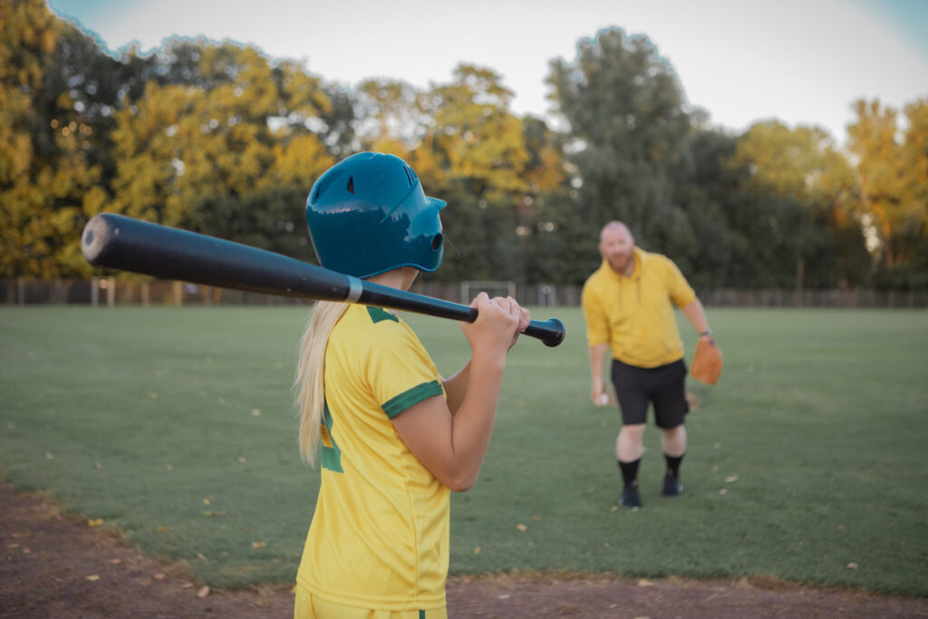 Middle Aged Redhead Father working hard during a baseball coaching session for his daughter at a training pitch on a sunny day